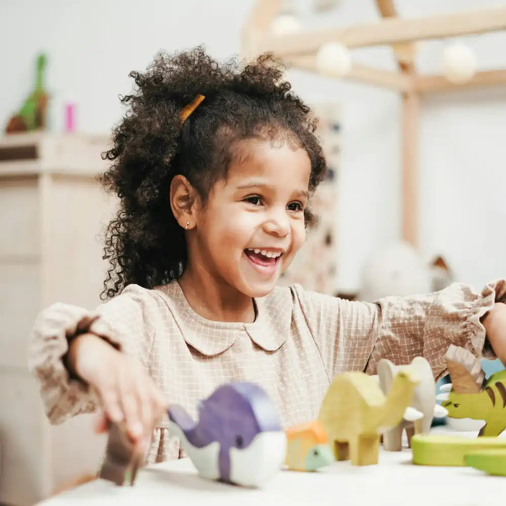 Happy child smiling and playing with colorful wooden toy animals on a table.
