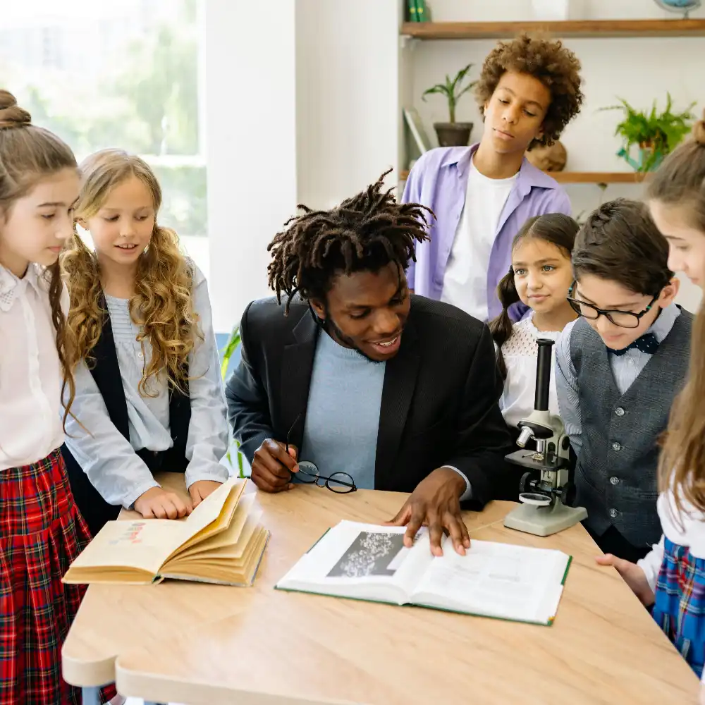 Teacher explaining a science lesson to students using books and a microscope in the classroom