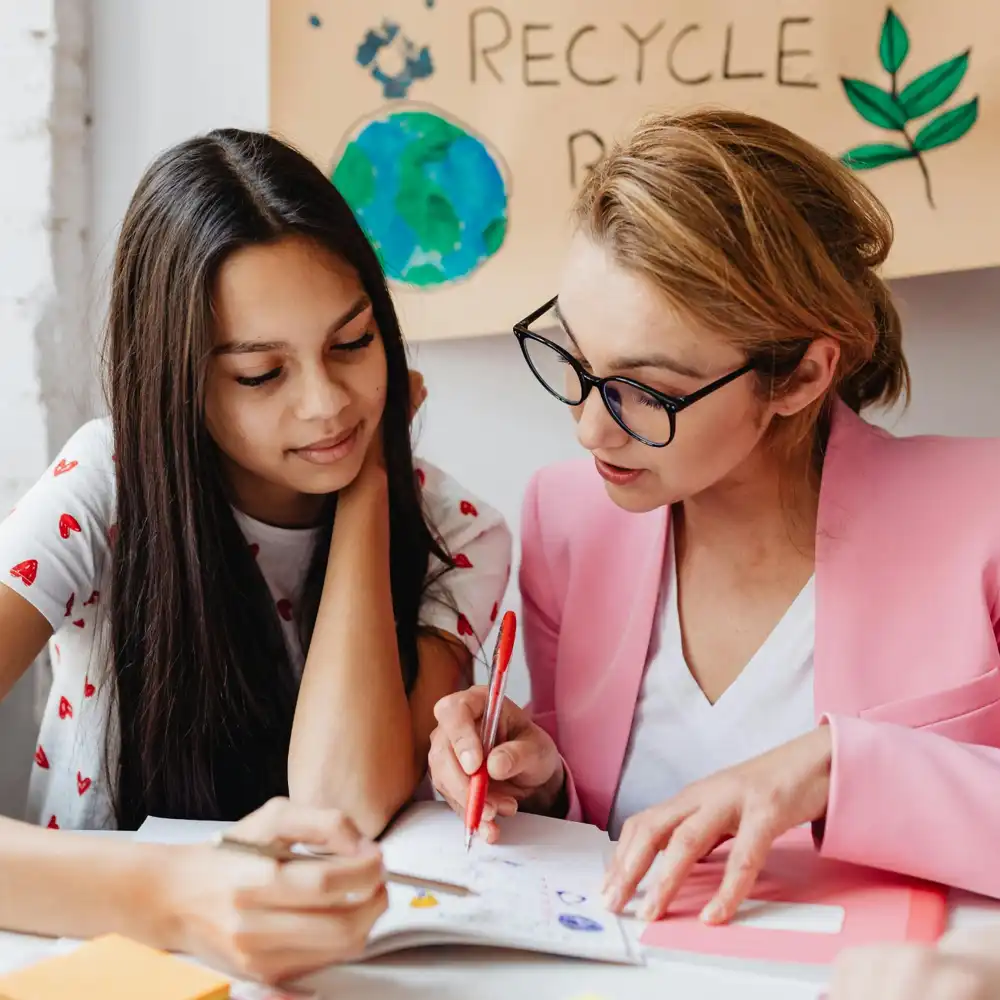 Teacher helping a teenage student with a creative school project on recycling and environmental awareness