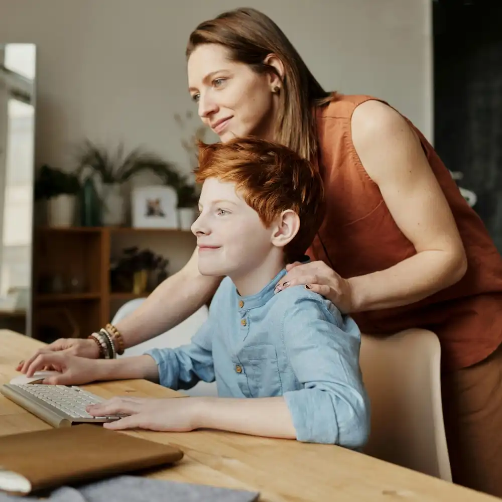 Tutor helping a child use a computer at home, providing learning support and guidance.